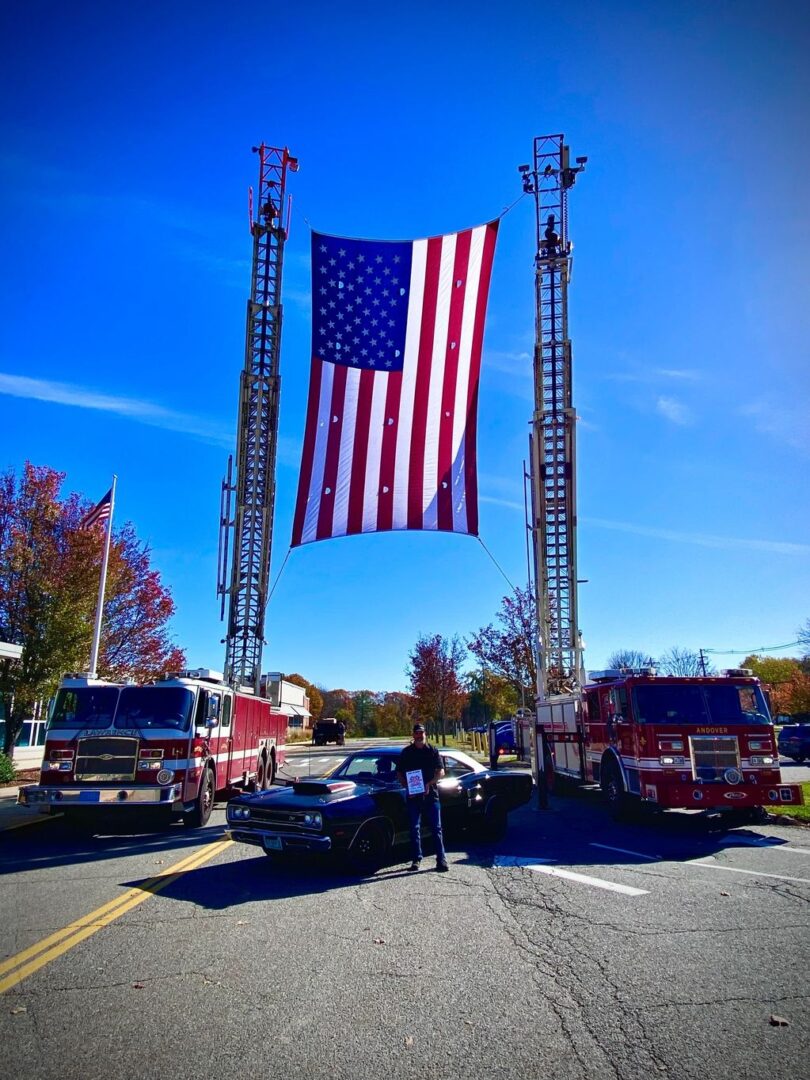 A large american flag hanging from two fire trucks.